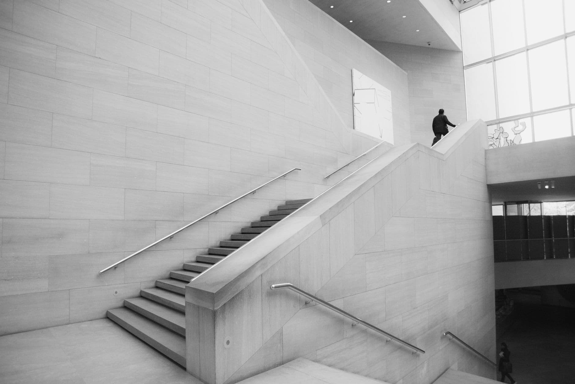 A modern museum staircase in pale stone, one figure ascending